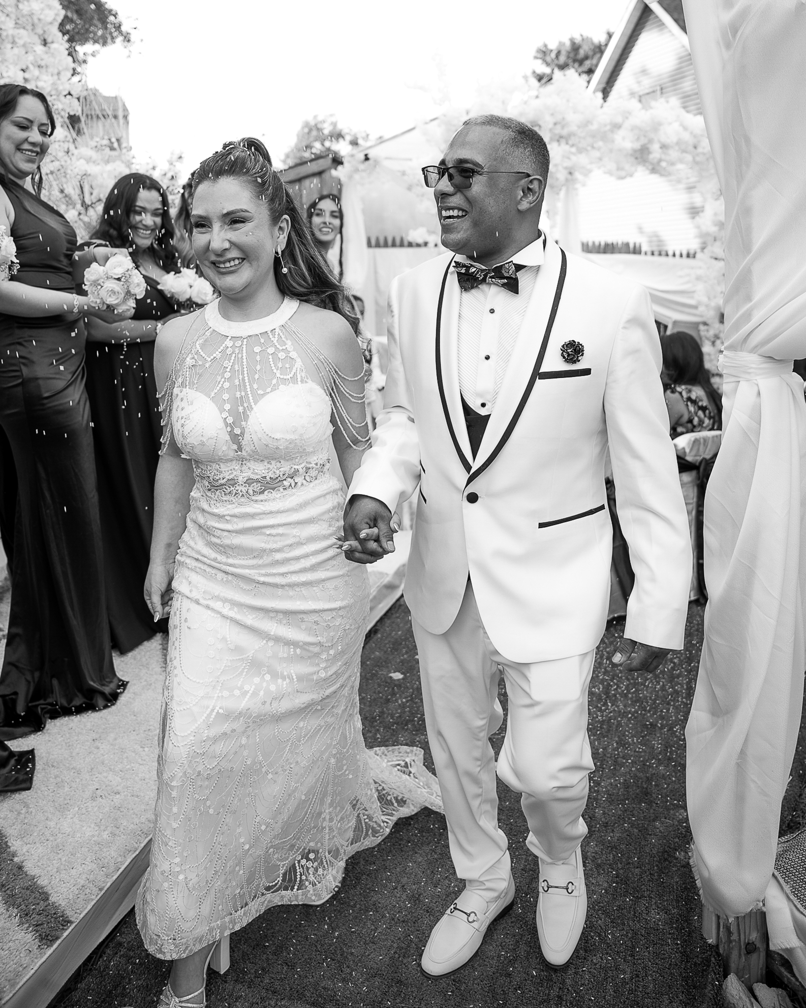 Pareja de recién casados saliendo de la iglesia, riendo mientras reciben una lluvia de arroz. Foto de boda en blanco y negro.