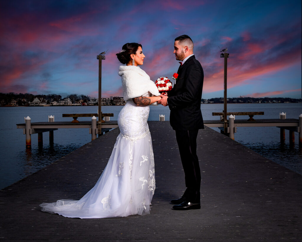 Fotografía de Boda Romántica al Atardecer en la Costa de New Jersey Pareja de boda tomados de la mano caminando en un muelle durante un atardecer sobre el mar en New Jersey. Imágenes de bodas románticas en la playa.