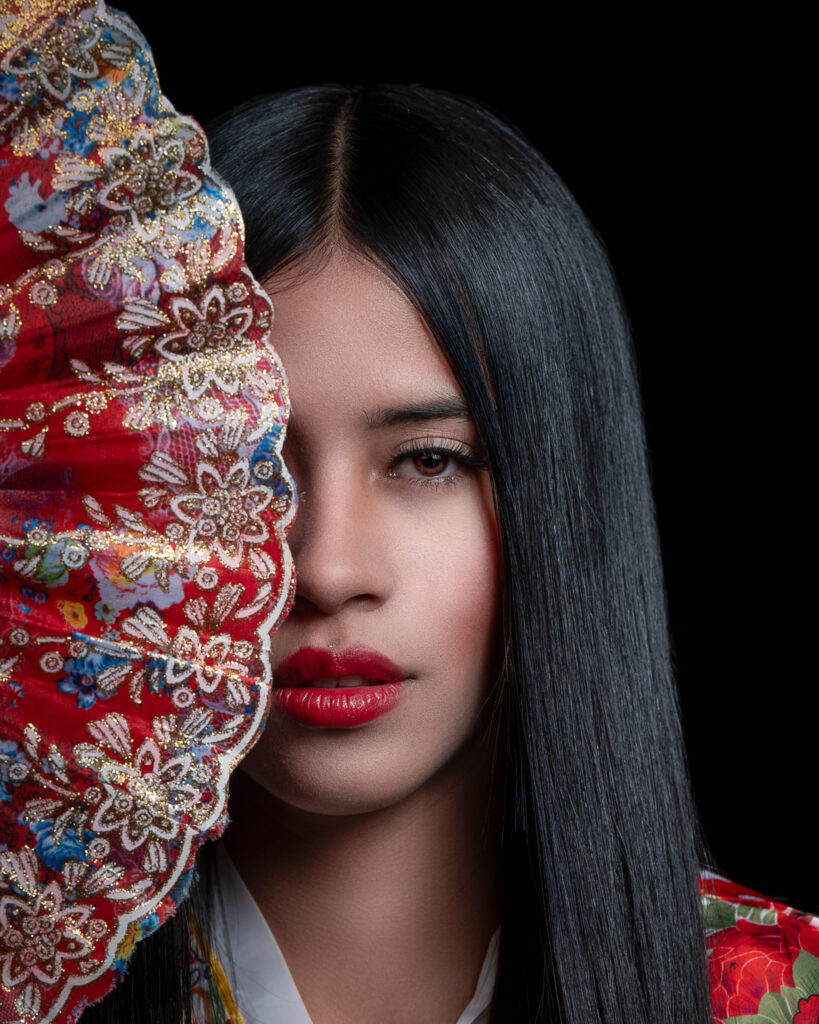 Sesión Fotográfica Artística en Estudio NJ | Geisha Cubriendo su Rostro con Abanico Fotografía de estudio en New Jersey de una geisha parcialmente oculta tras un abanico. Retrato creativo con enfoque en el misterio y la elegancia.